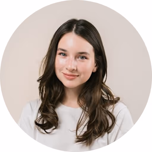 Smiling young woman with long brown hair wearing a white shirt against a beige background.