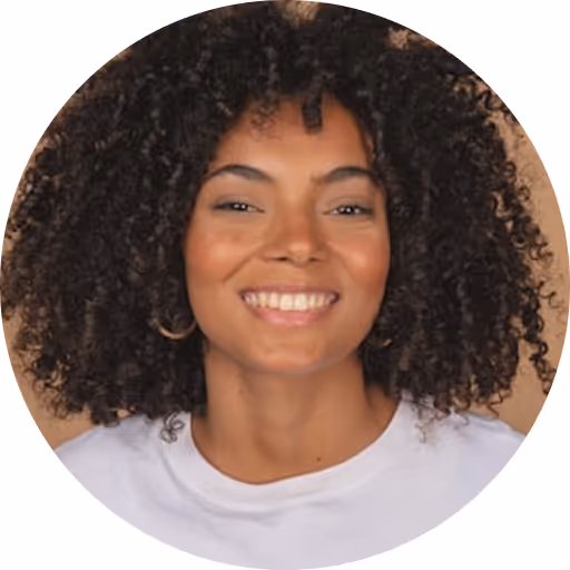 Smiling young woman with curly hair wearing a white shirt and hoop earrings against a beige background.
